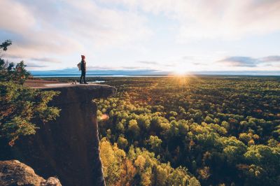 A person standing on a cliff overlooking a forest landscape