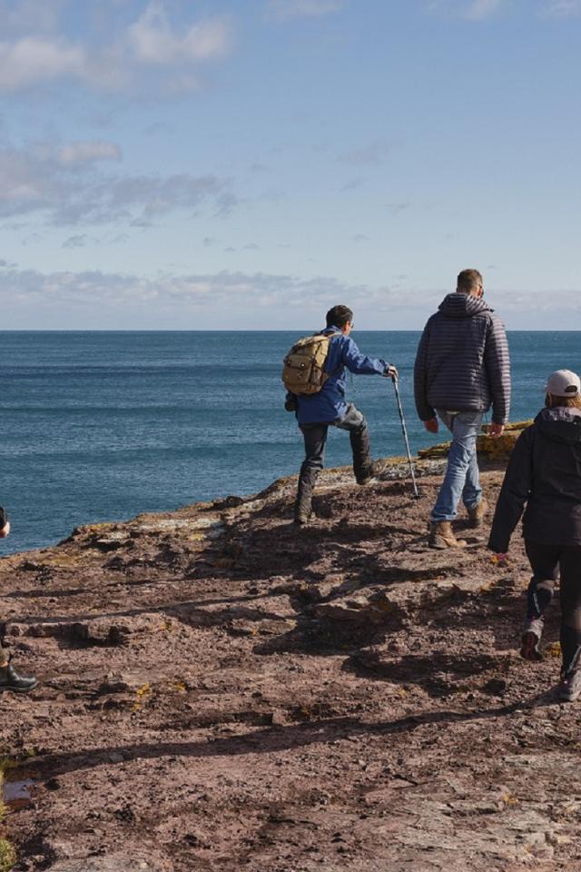 Quatre personnes marchent le long d’une falaise rocheuse qui donne sur l’océan.
