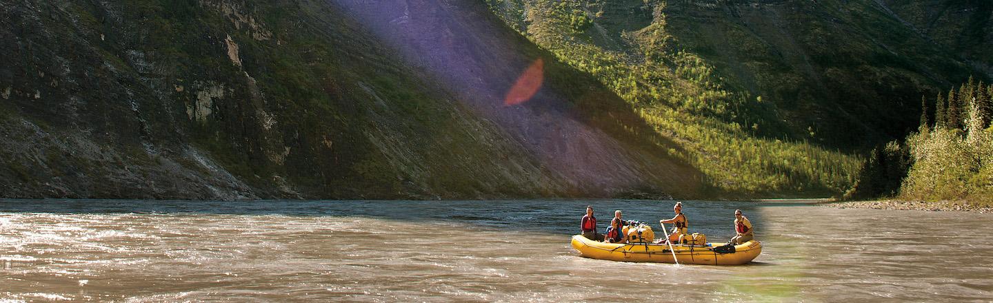 Group of people in a yellow raft on a river with mountains in the background