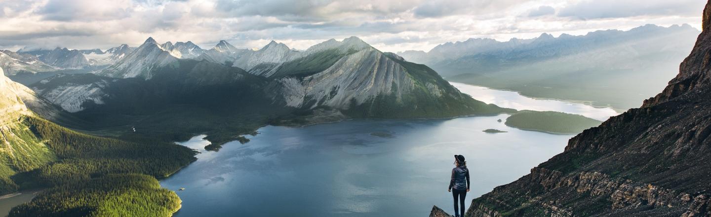 solo hiker stands on rocky outcrop overlooking a lake and mountains