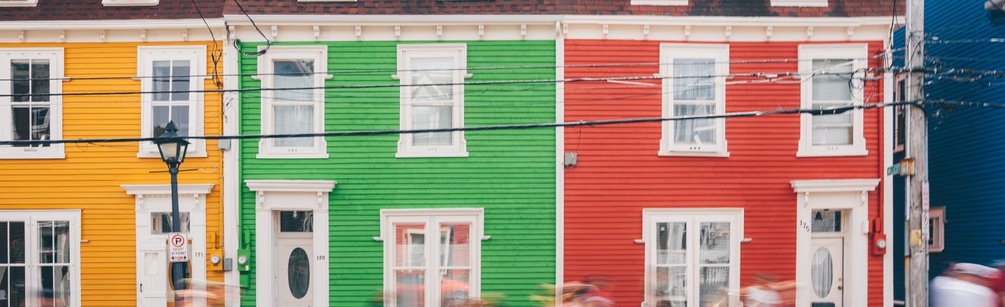 Des gens floutés marchent devant des bâtiments colorés.