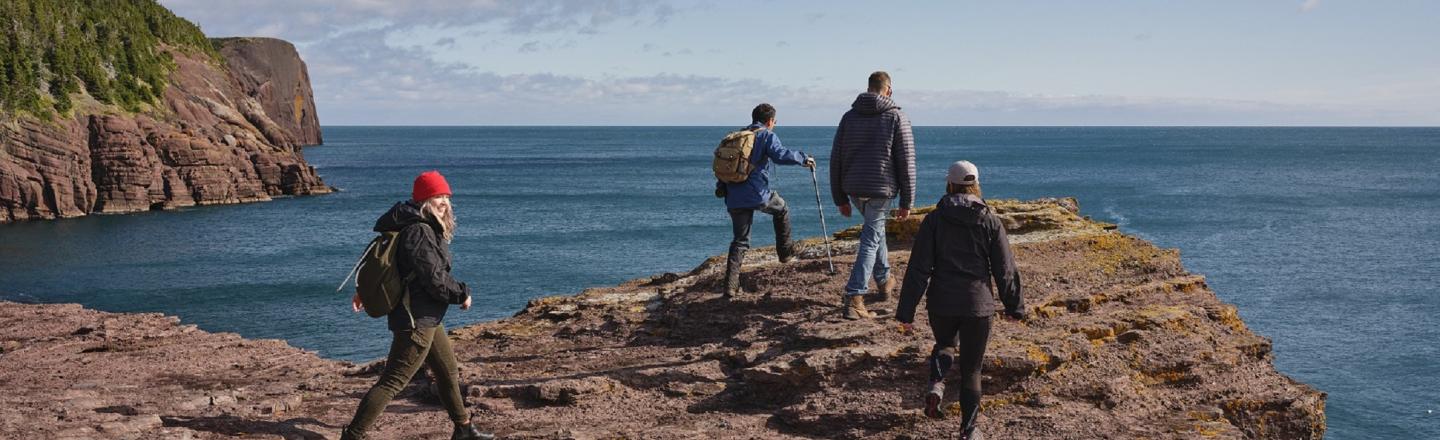 Four hikers walking along a rocky coastal cliff overlooking the ocean