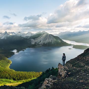 solo hiker stands on rocky outcrop overlooking a lake and mountains