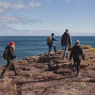 Four hikers walking along a rocky coastal cliff overlooking the ocean